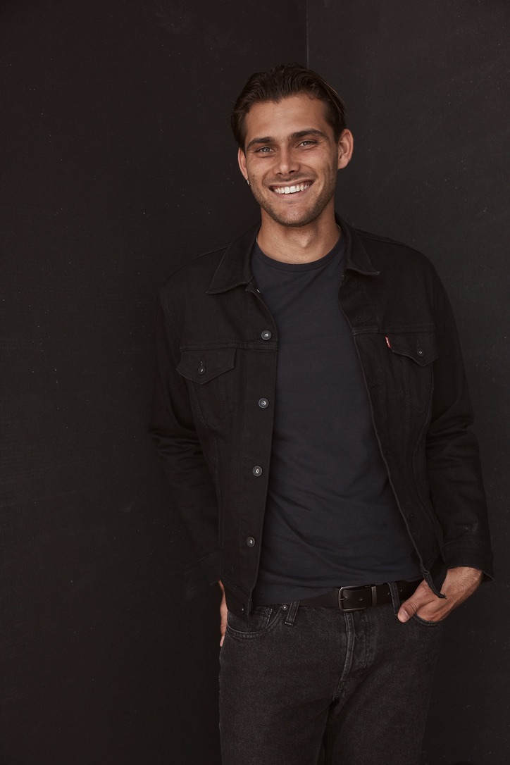 Asgard Bishop in a black denim jacket, smiling, against a dark studio wall